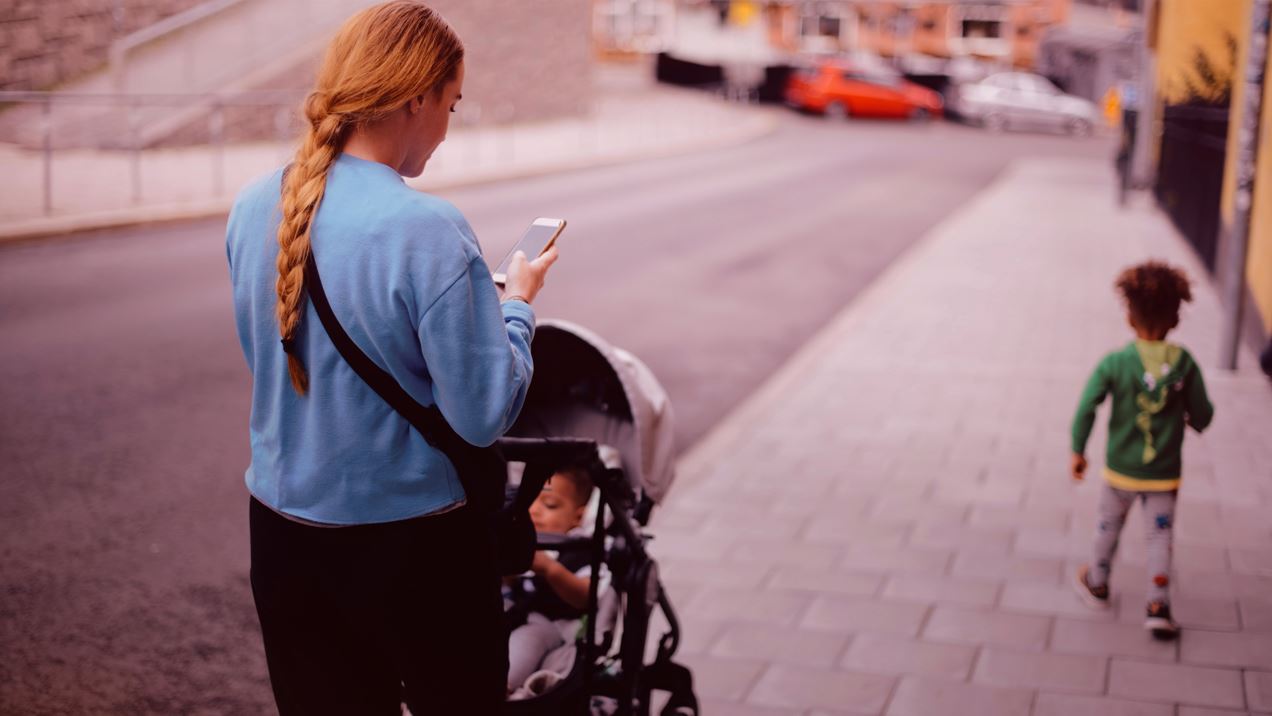 Kvinna med barnvagn tittar ner i sin mobiltelefon.