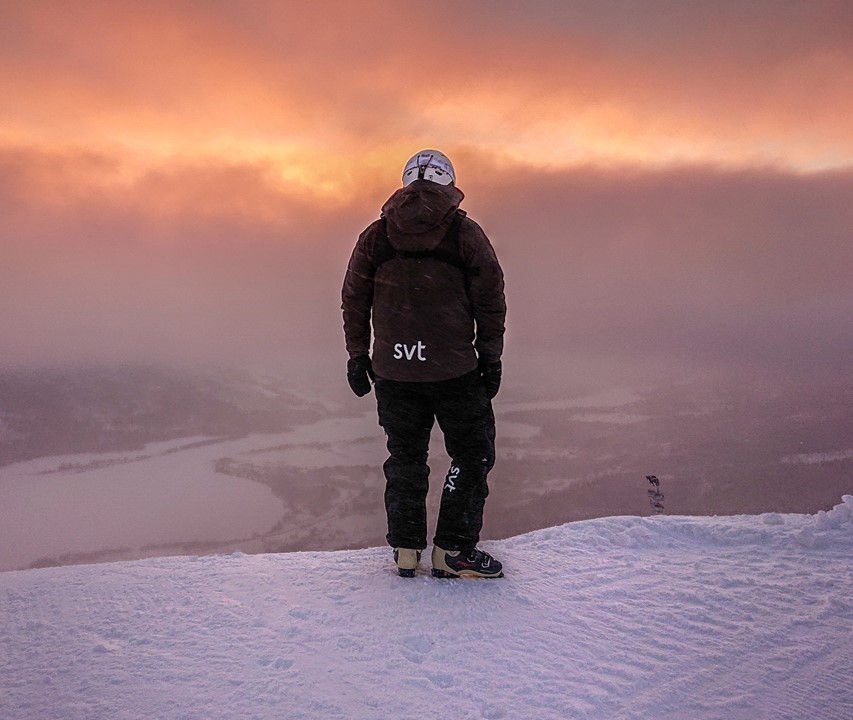 En ensam man med mörk täckjacka med svt-logga på står i ett snöigt landskap, vänd med ryggen mot kameran. Foto: Jan Danielsson/SVT